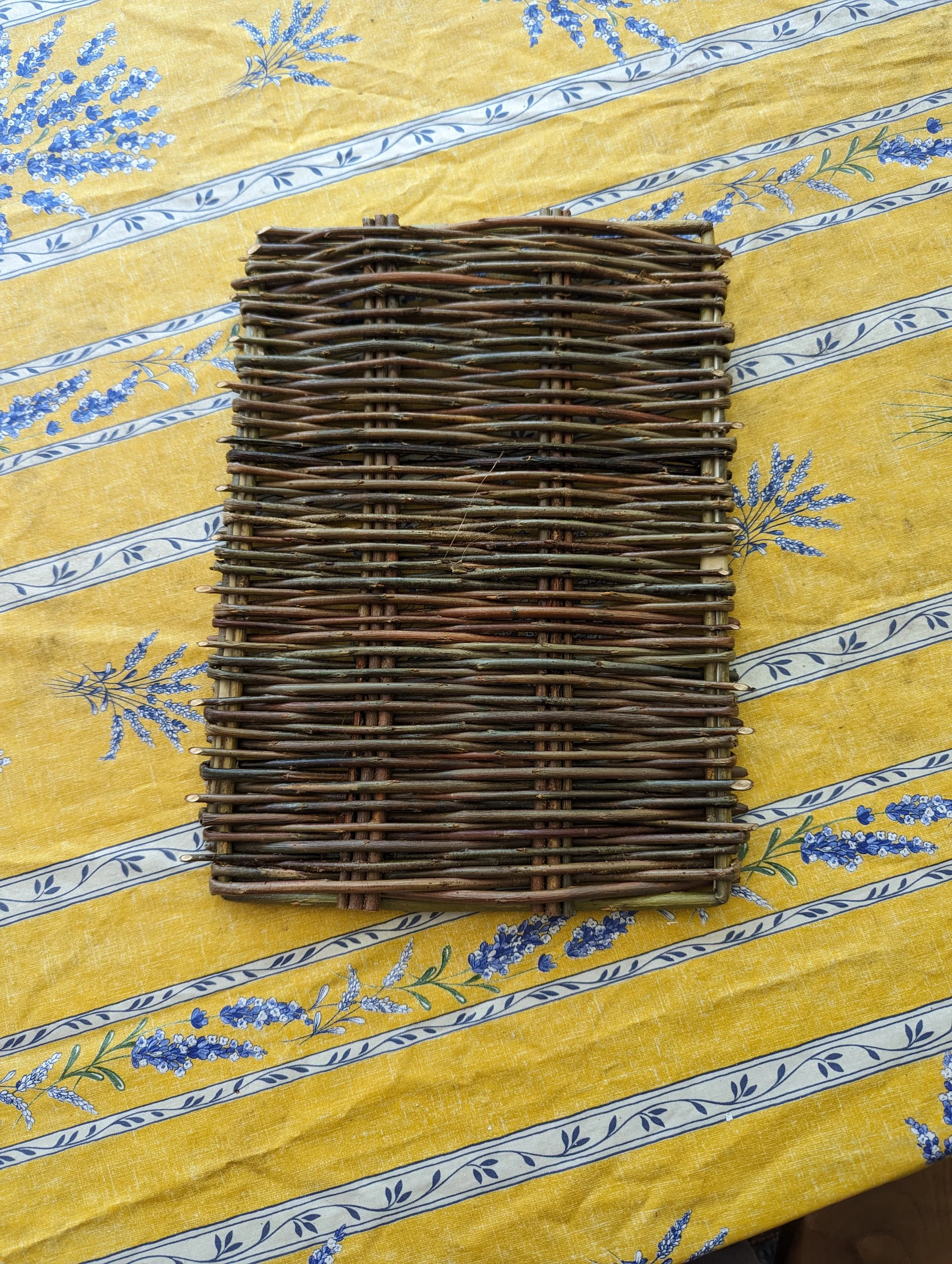 A woven willow trivet tray on a yellow tablecloth with blue floral patterns.