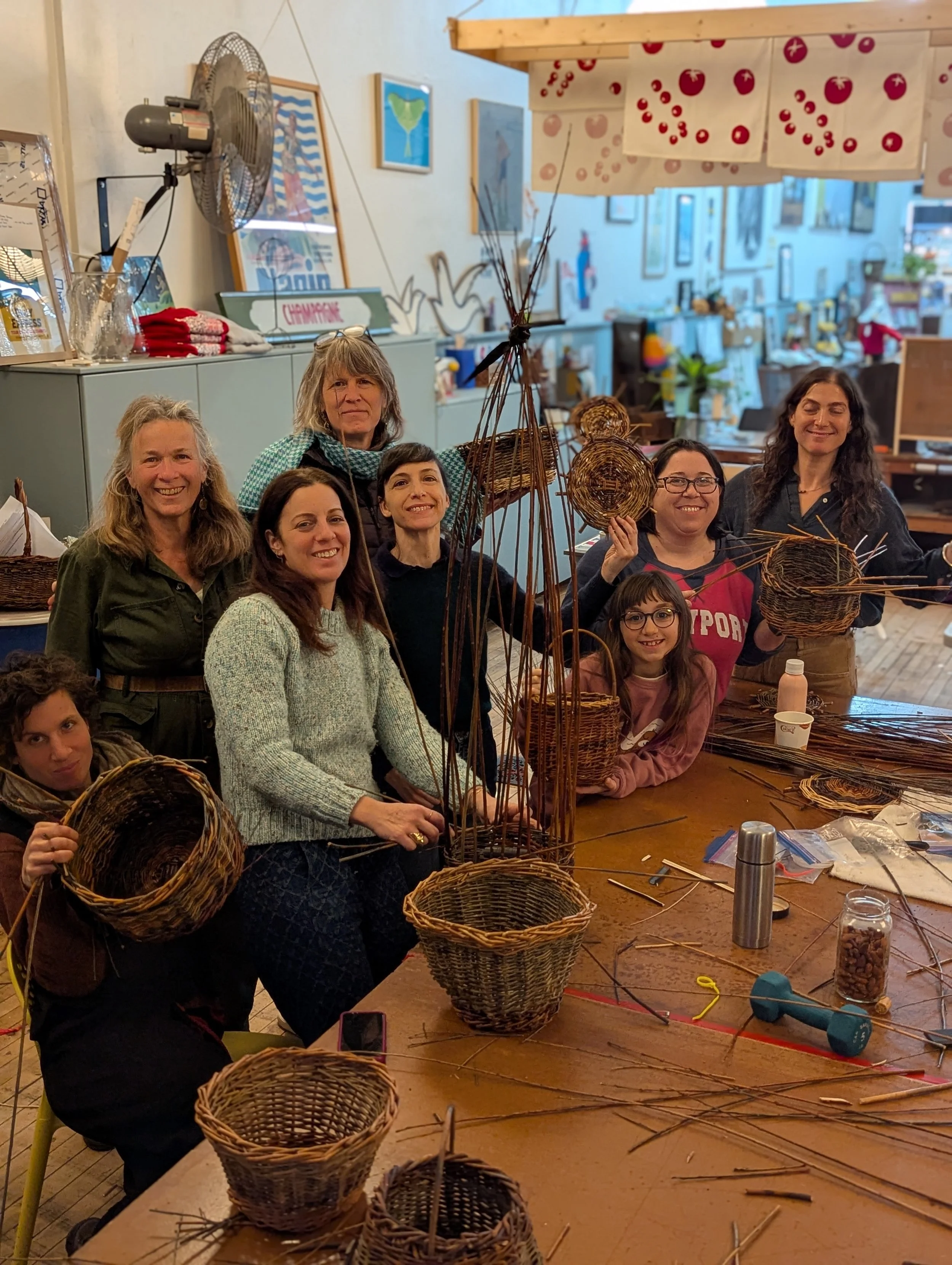 A group of people gathered around a table making wicker baskets in a craft workshop.