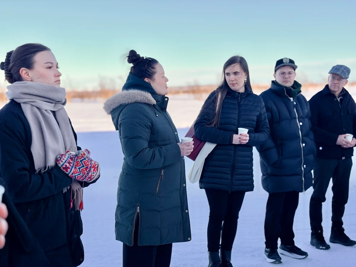 Five people talking outdoors on the snow, wearing winter coats and holding warm drinks