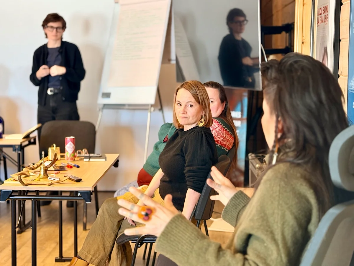 Participants listening during a workshop discussion, with a flip chart and traditional Sámi objects on a table nearby