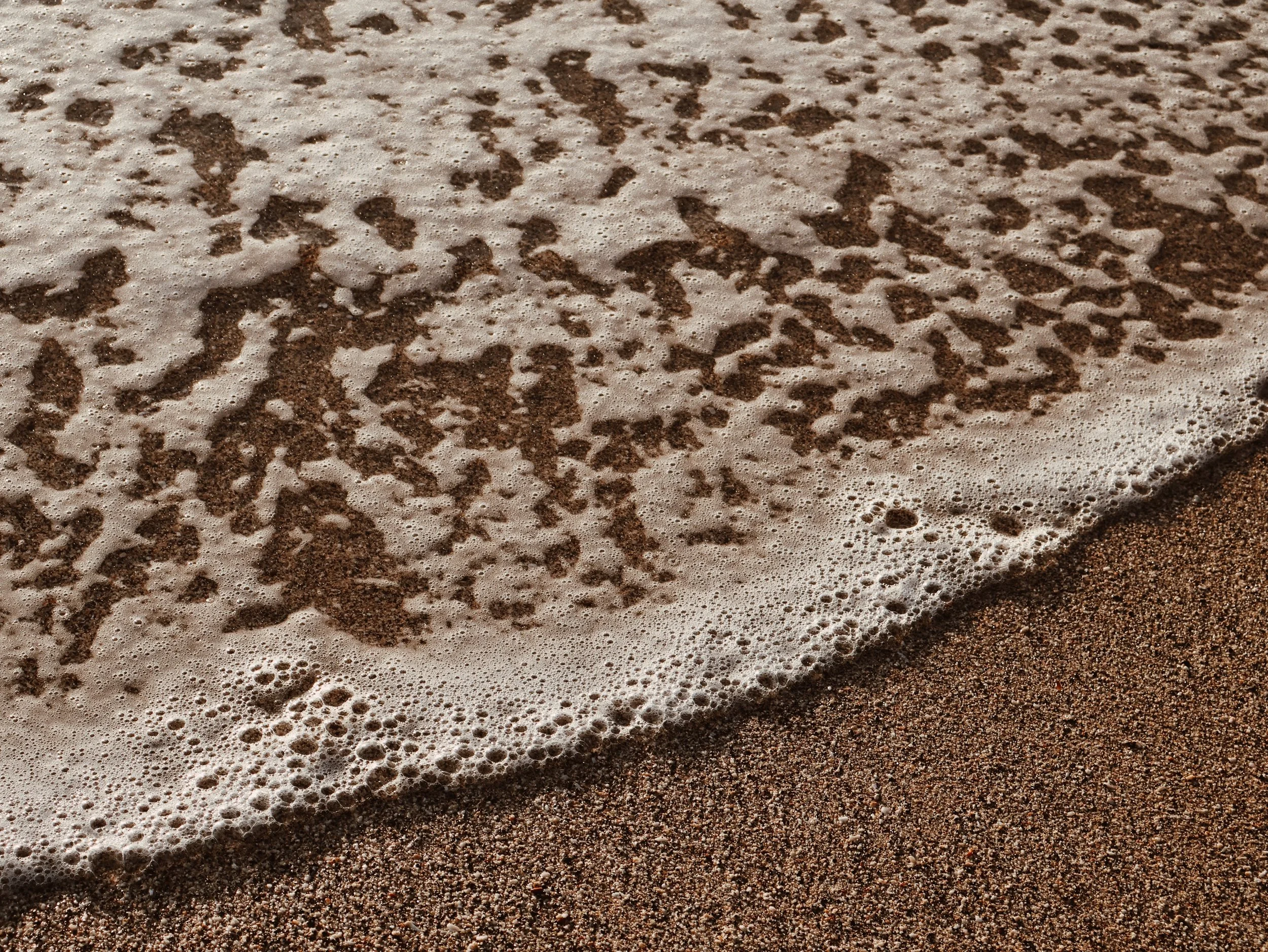 Close-up of foamy sea waves on sandy beach.