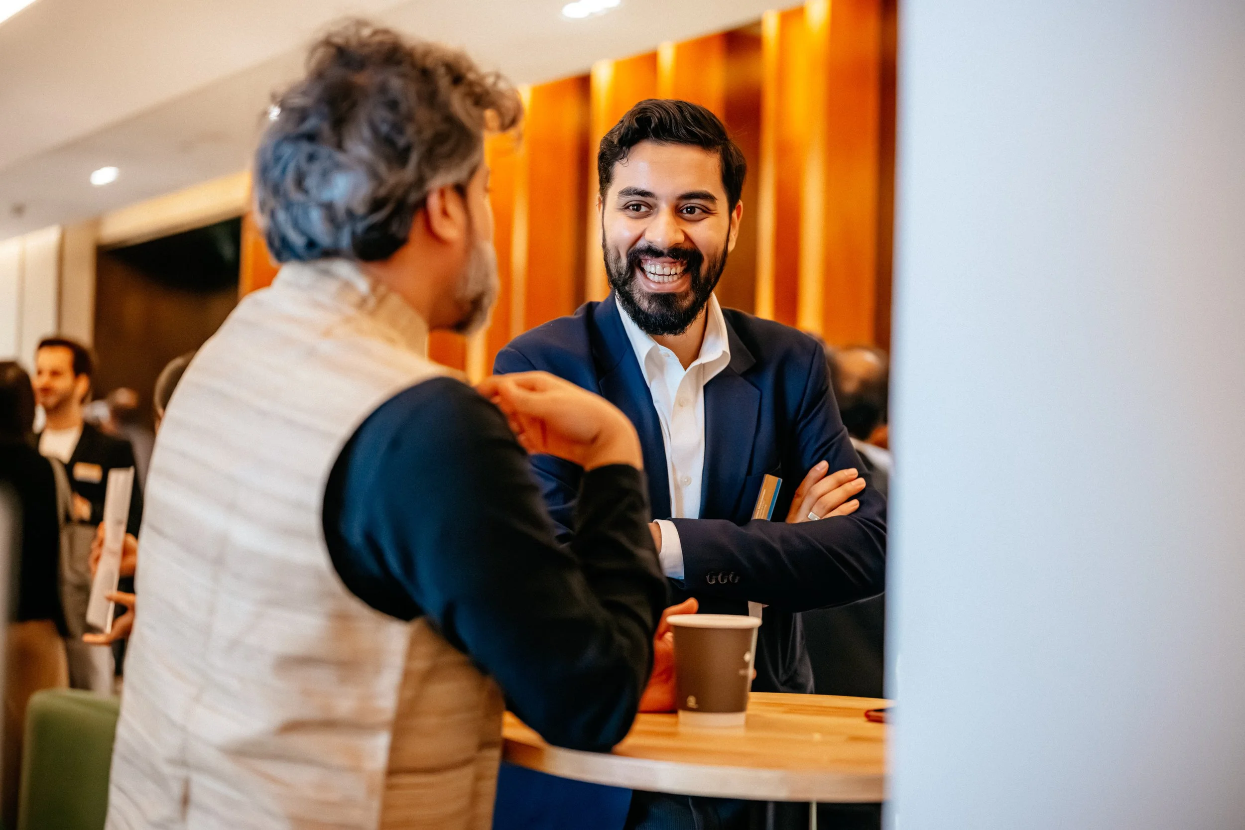 Google Ai Summit - Two men talking at a table during a professional event or conference, one with gray hair and the other with dark hair and a beard, both smiling. Captured by James Bridle Event Photographer. 