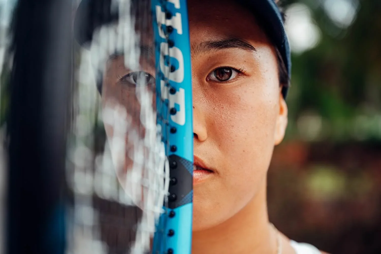 Dunlop Sports Campaign by James Bridle Photography, A person holding a blue tennis racket, with one side showing their face and the other side showing their reflection in the racket's surface.