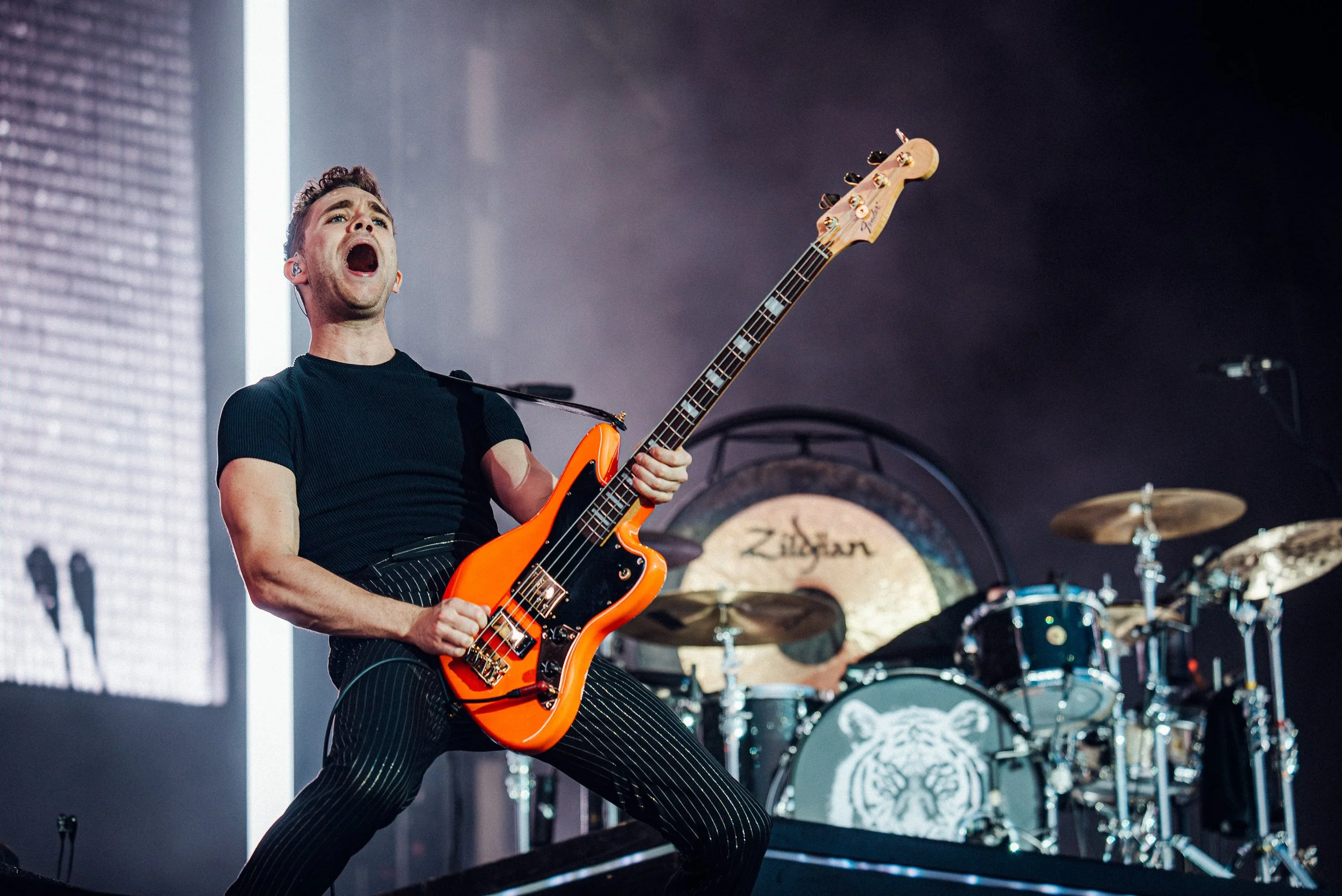 Royal Blood at Reading 2019 Captured by James Bridle Music Photographer the photo shows Mike Kerr holding an orange electric bass guitar, with a large drum set in the background featuring a tiger logo on the bass drum.