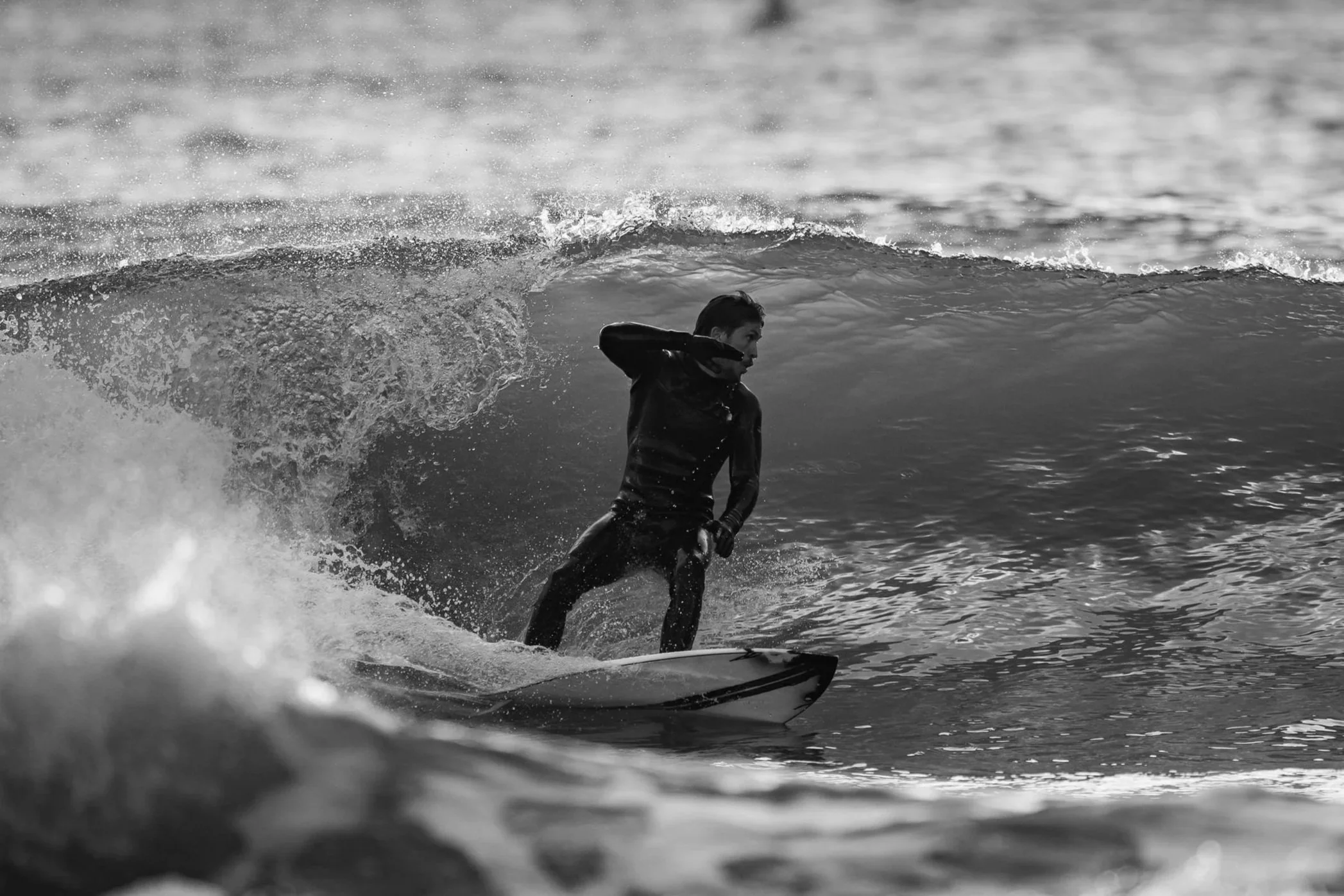 A person waves while surfing on a wave in black and white. taken at Bournemouth Pier by James Bridle UK
