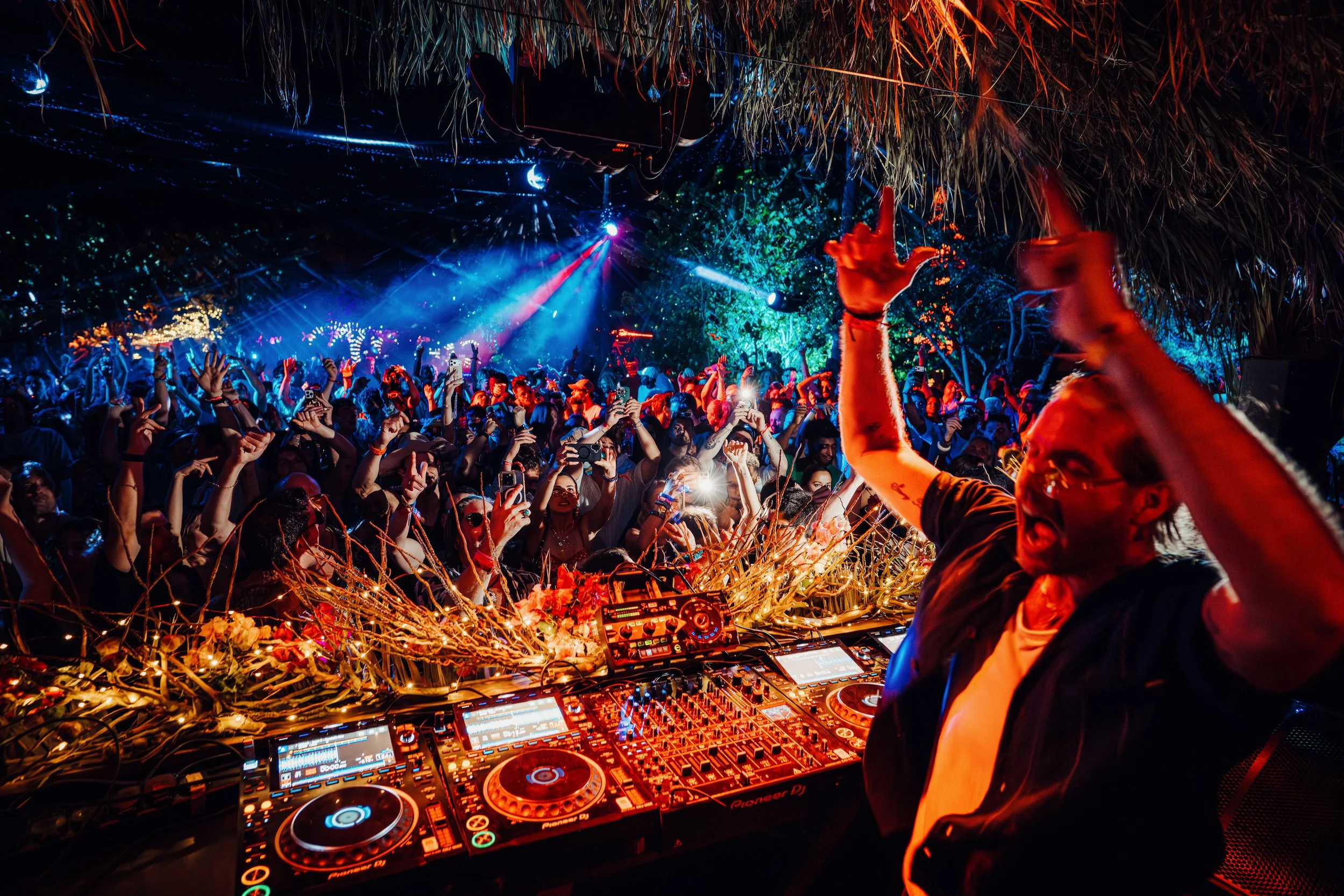 &friends performing at SXM Festival Ocean Stage with a crowd dancing under colorful lighting and decorative natural elements in the background. by James Bridle Music Photographer 2026 