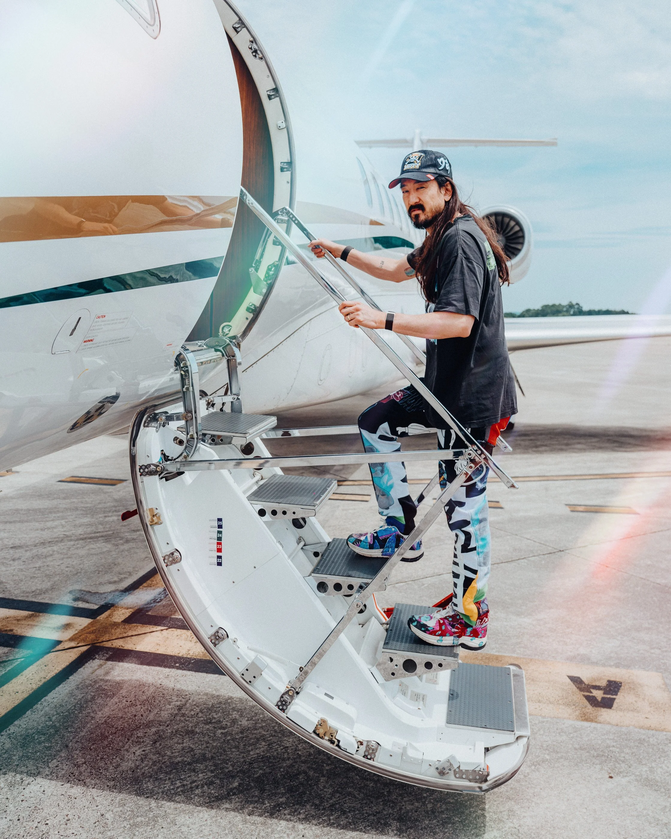 Man in colorful pants and sneakers boarding a private jet via stairs on the tarmac.