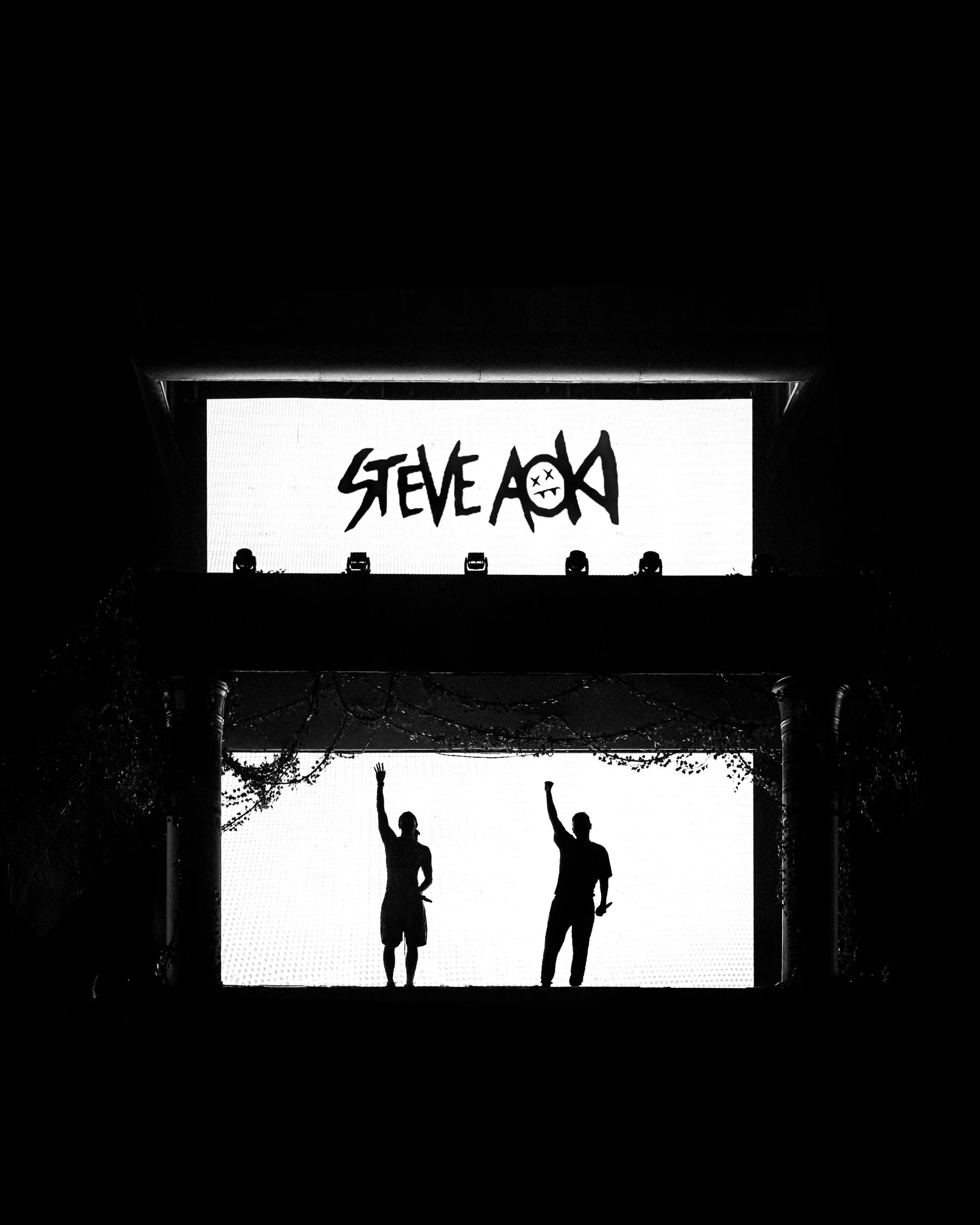 Steve Aoki & Dimitri Vegas B2B on stage waving with large screens behind them displaying 'Steve Aoki' and a smiley face logo taken in Valencia. 