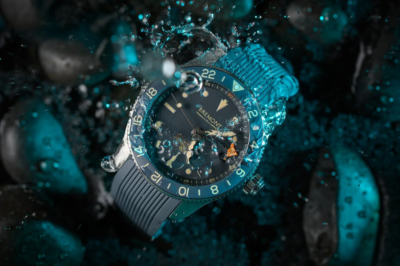 A Bremont wristwatch submerged underwater among rocks and pebbles, with water splashing on its surface.