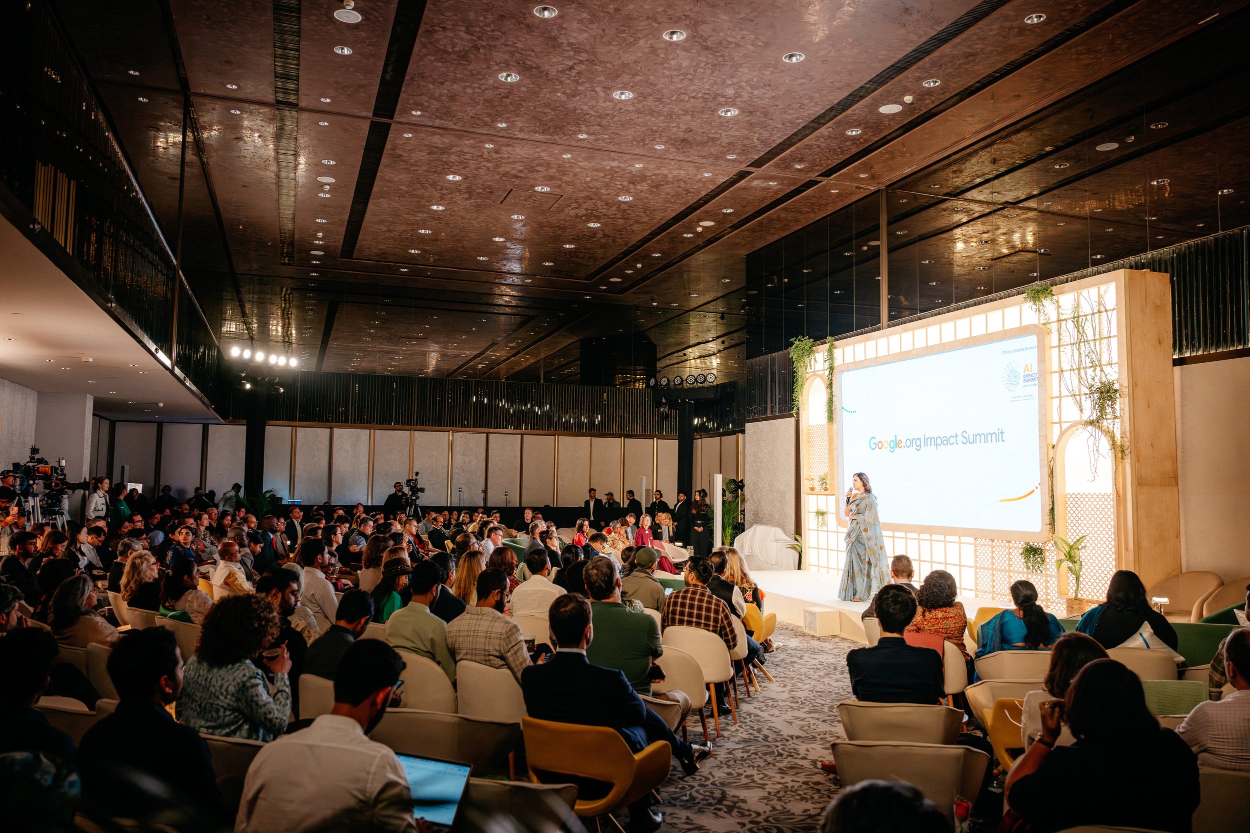 Dia Mirza on stage speaking at the Google.org Impact Summit, with a large screen behind her displaying event branding, and a seated audience listening. Captured by James Bridle Event Photographer