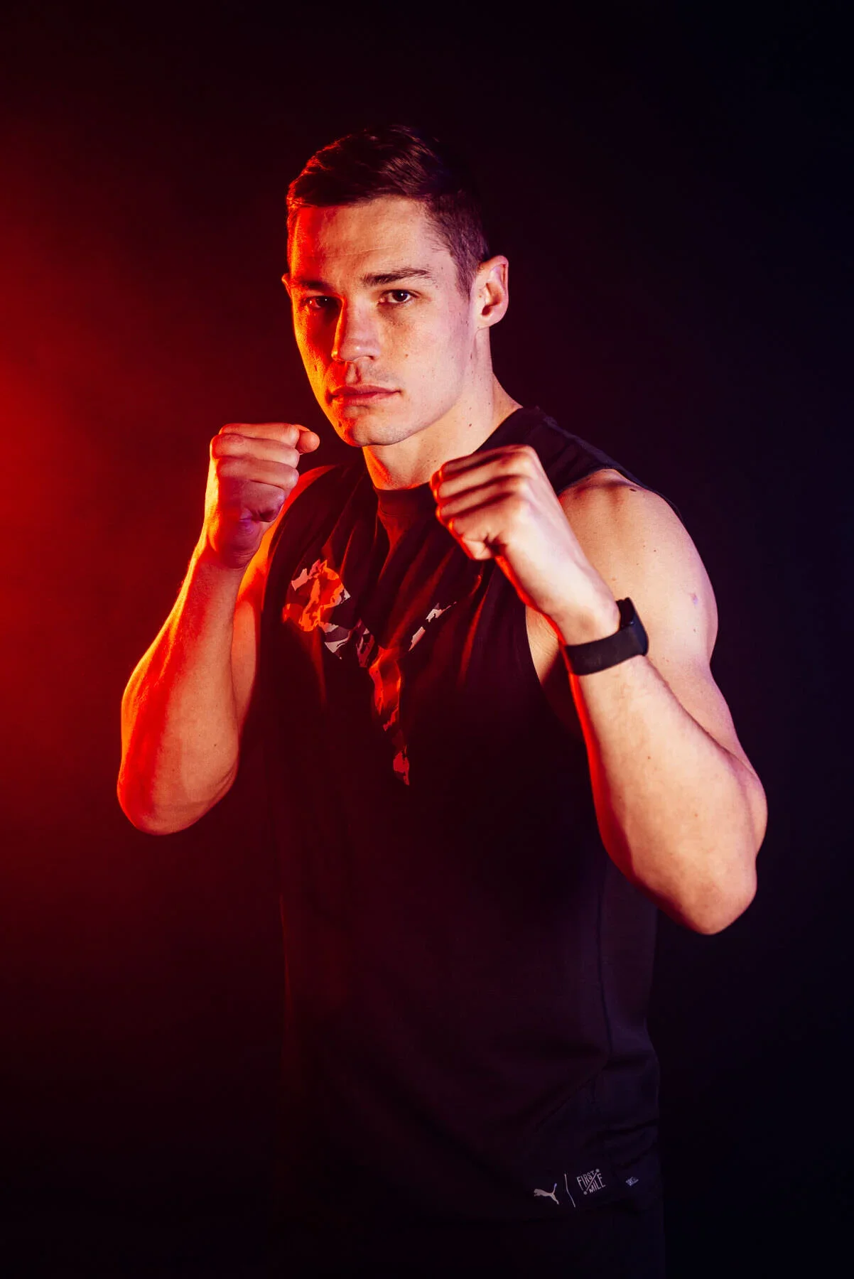 Chris Billham Smith Boxer - A young man in athletic wear posing with fists raised in a boxing stance, black background, red and orange lighting.
