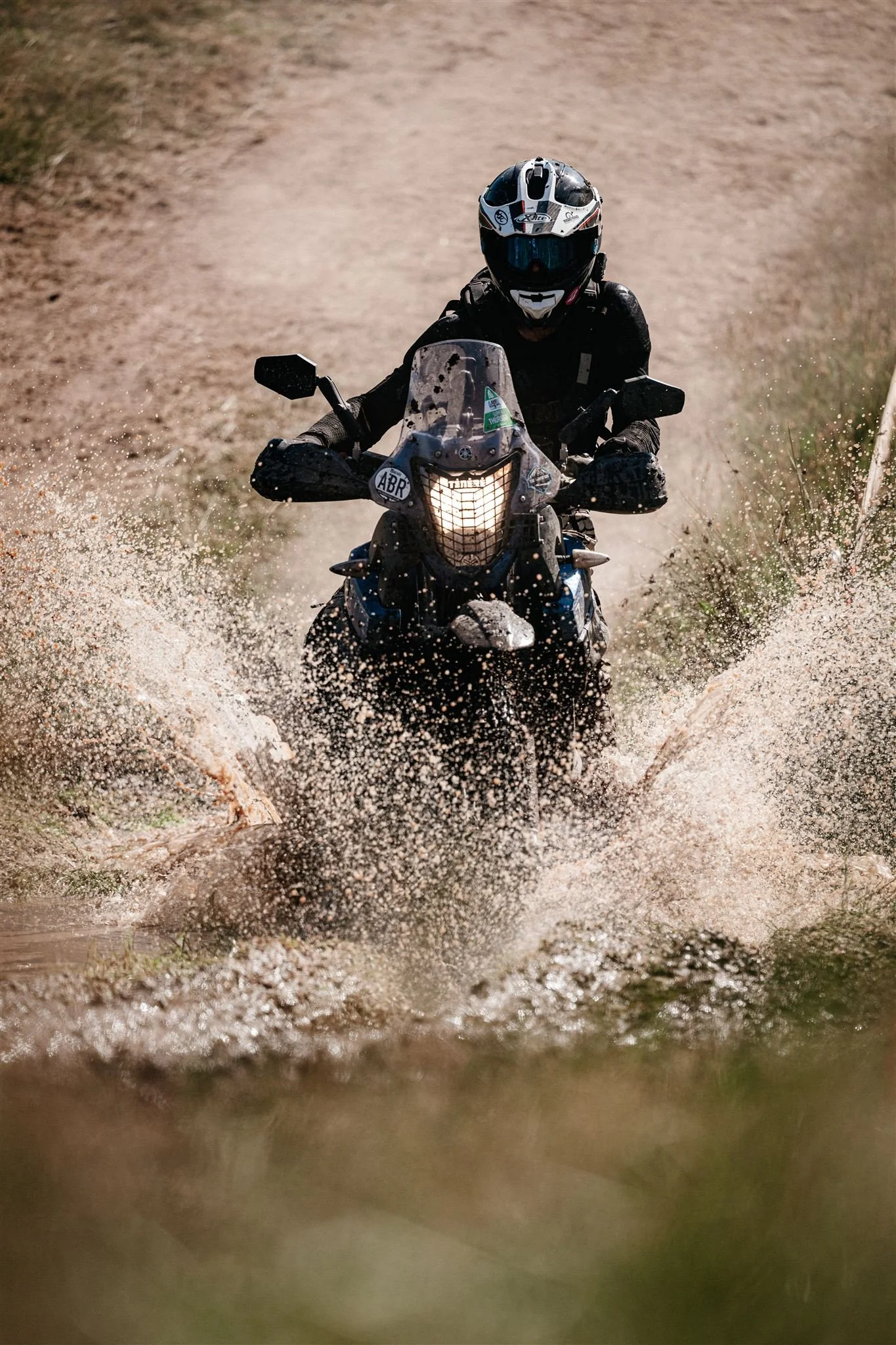 Motorcyclist riding through a shallow water crossing on a dirt trail.