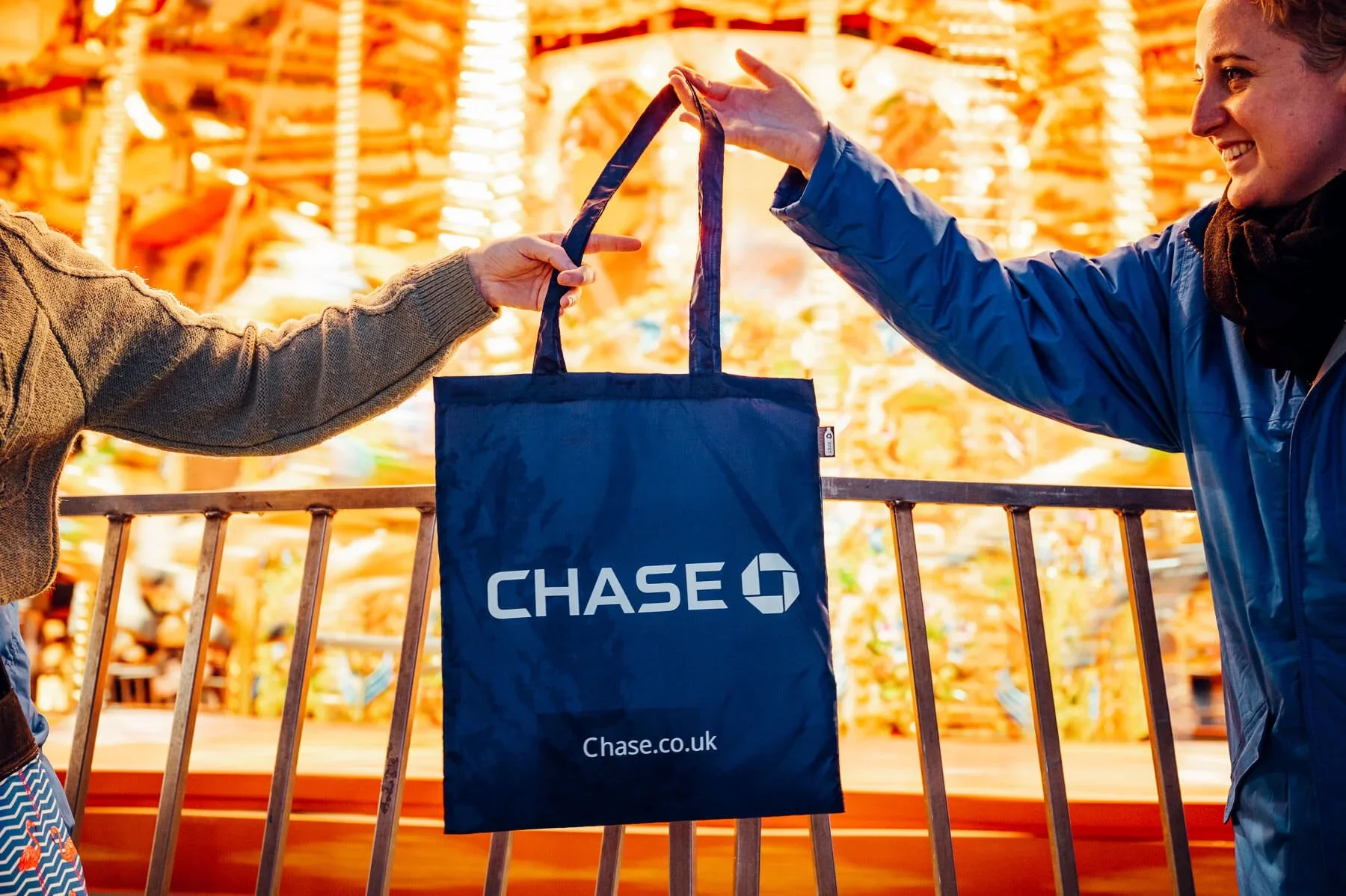 Chase Christmas Commercial - Two people exchanging a Chase branded tote bag at a bright, colorful indoor location with wooden decor.