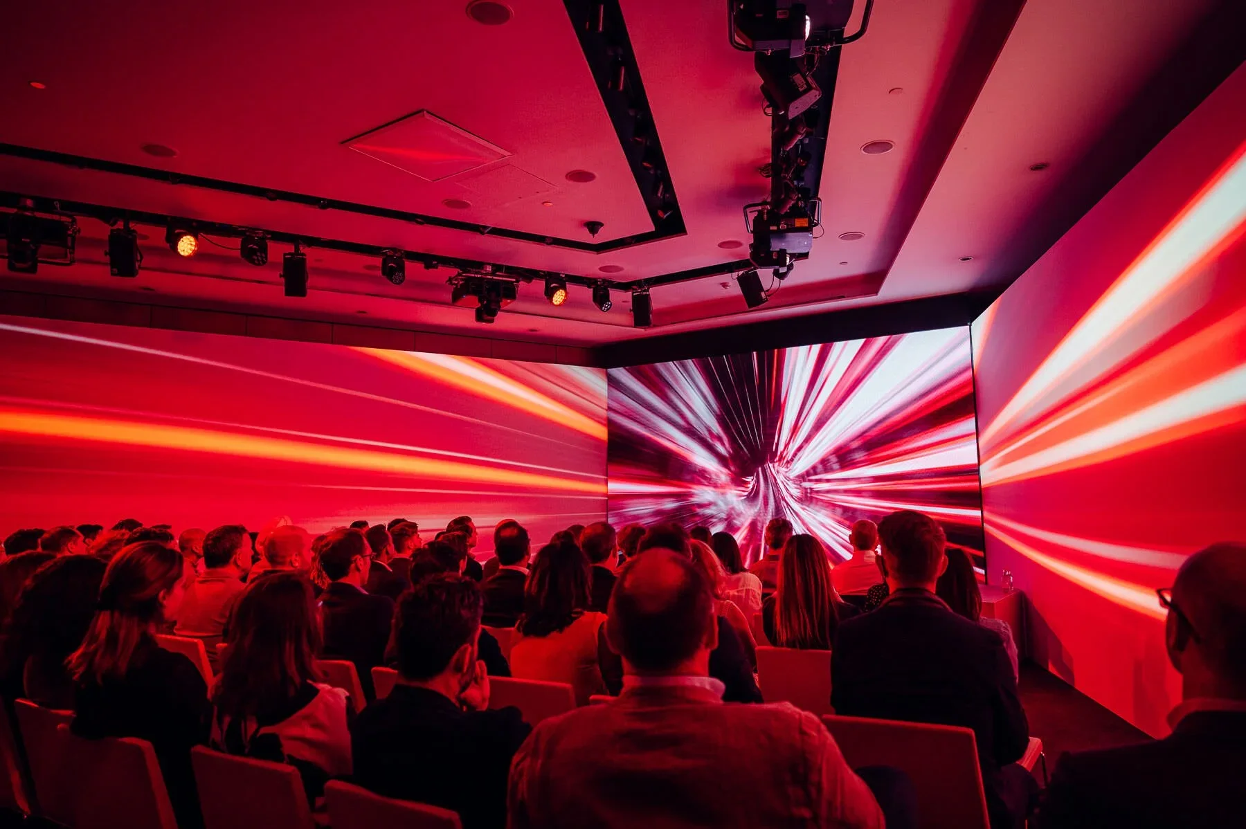 Virgin Media Launch their streaming Option. Shot as part of Audience London shows people seated watching a presentation or movie on a large digital screen displaying a red abstract background with streaks of light.