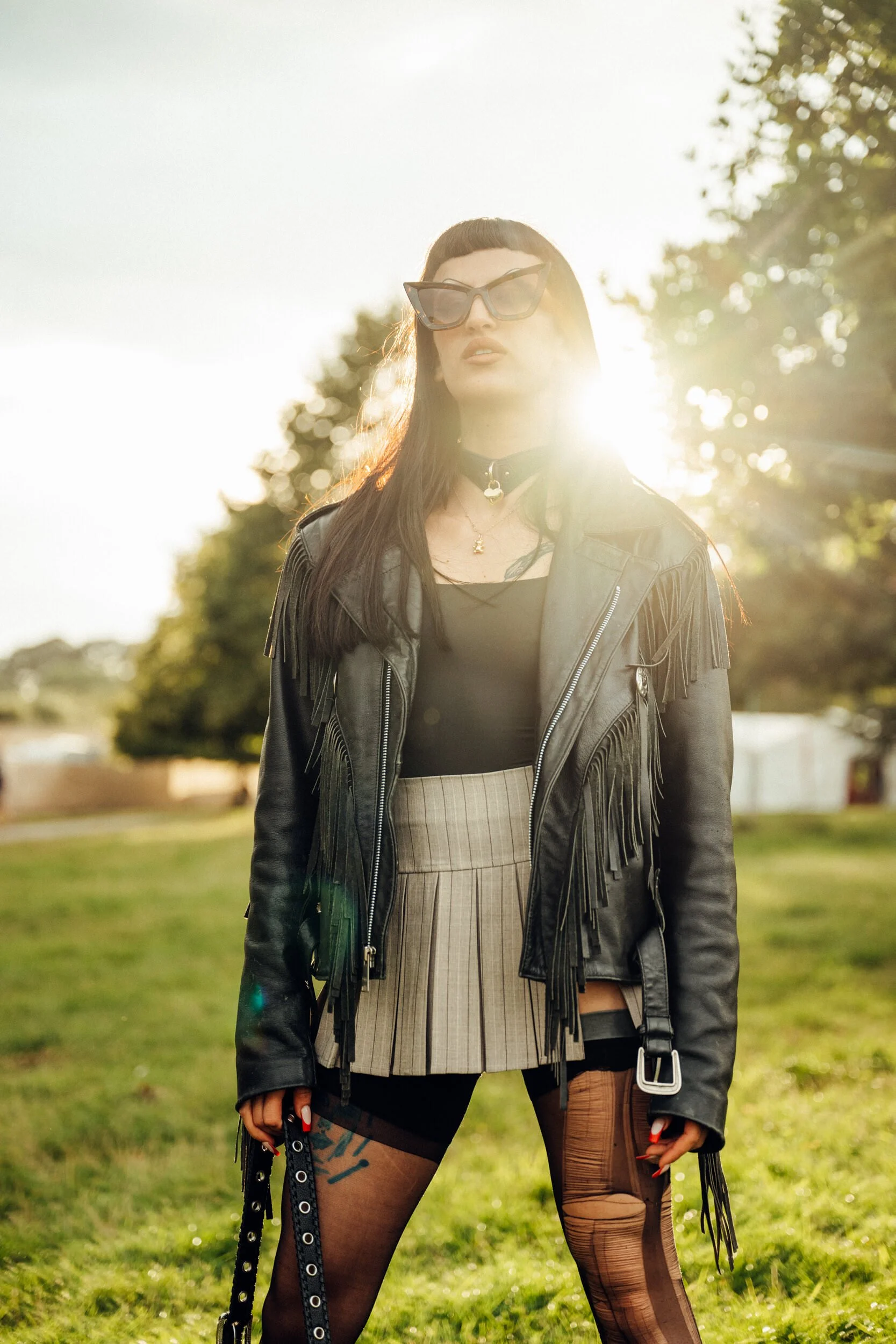 Wilderness Festival 2023 taken by James Bridle Photography showing a woman in Black Leather with the sun behind her, she has dark shades and is posing to camera. 