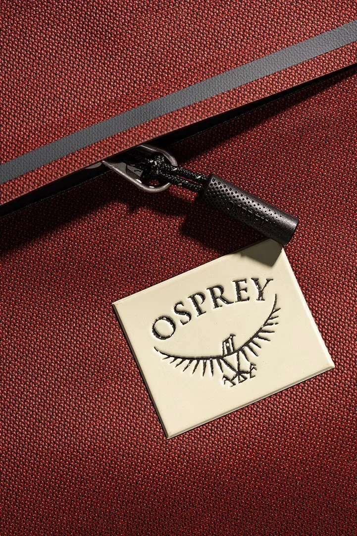 Product Photography close-up of a red textured suitcase with a Osprey luggage tag attached to a black zipper.