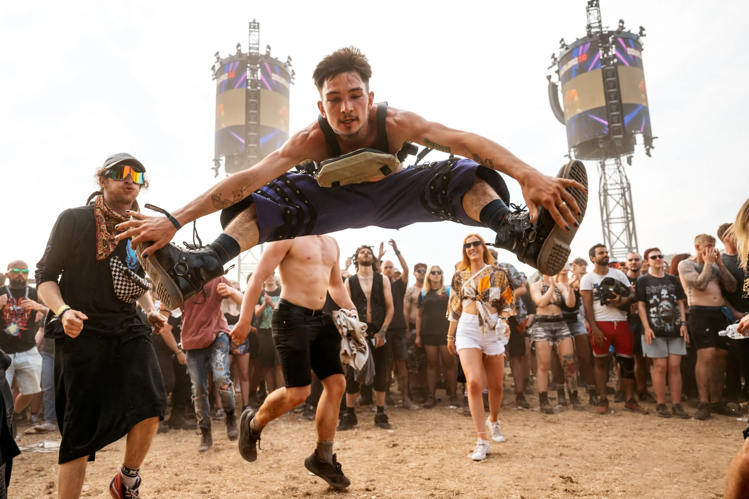Download Festival Goer jumping in front of a crowd at an outdoor music festival, others watching, stage towers in the background. Captured by James Bridle 2024
