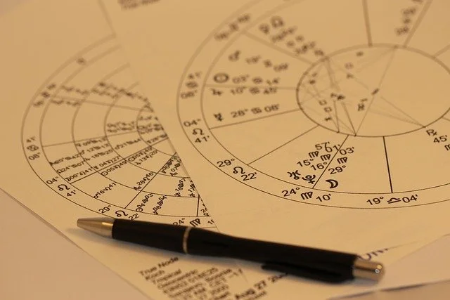 Two sheets of paper with detailed astrological charts and a black pen on top.