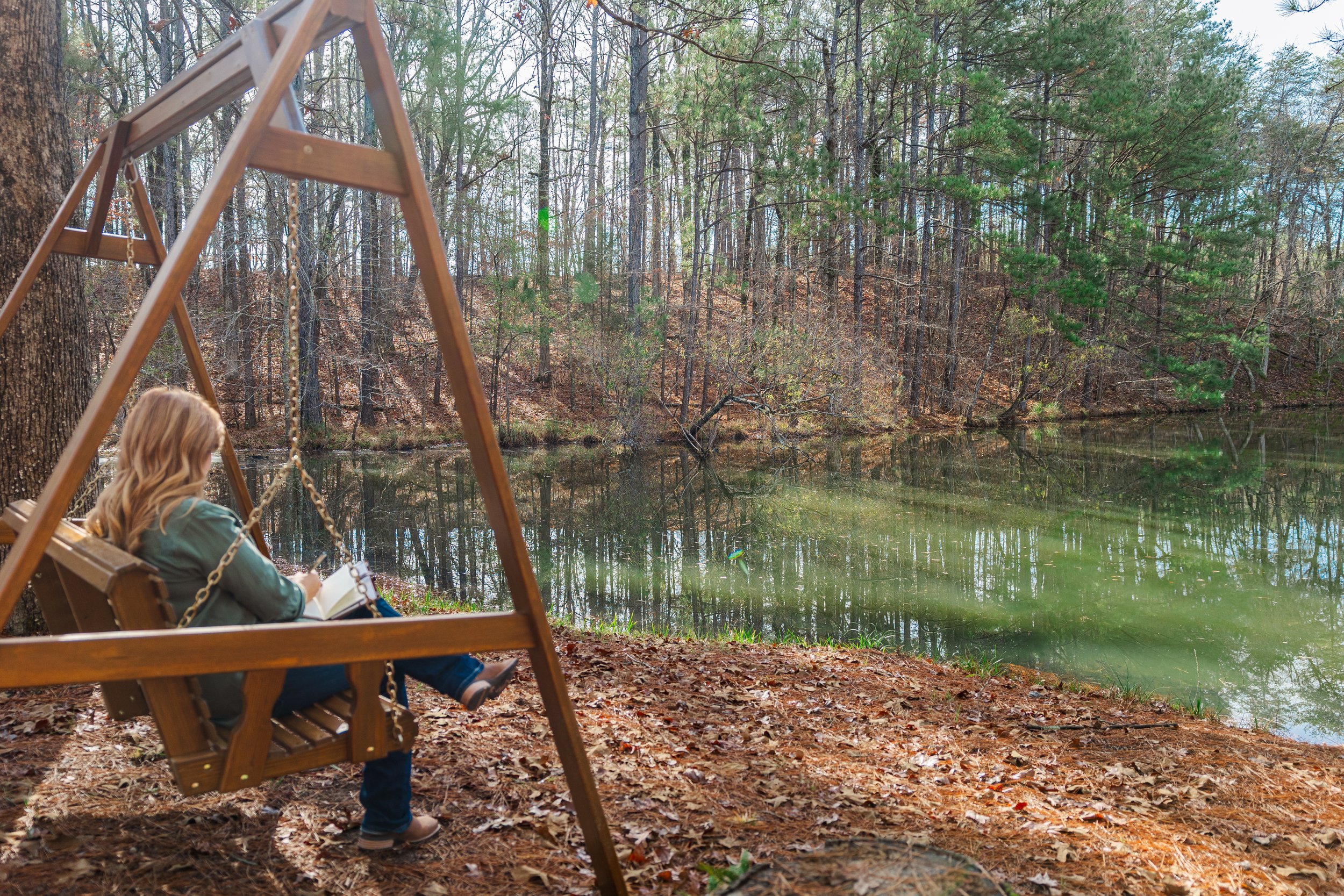 Deidre King, Certified LifePlan Guide, sitting on a peaceful swing overlooking the lake in an Alabama forest during a reflective moment.