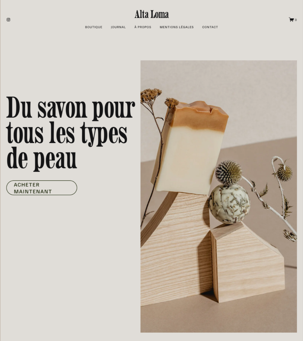 Une photo d'une boutique en ligne de savon artisanal, avec un savon beige et blanc posé sur un support en bois, entouré de plantes sèches et de fleurs décoratives.