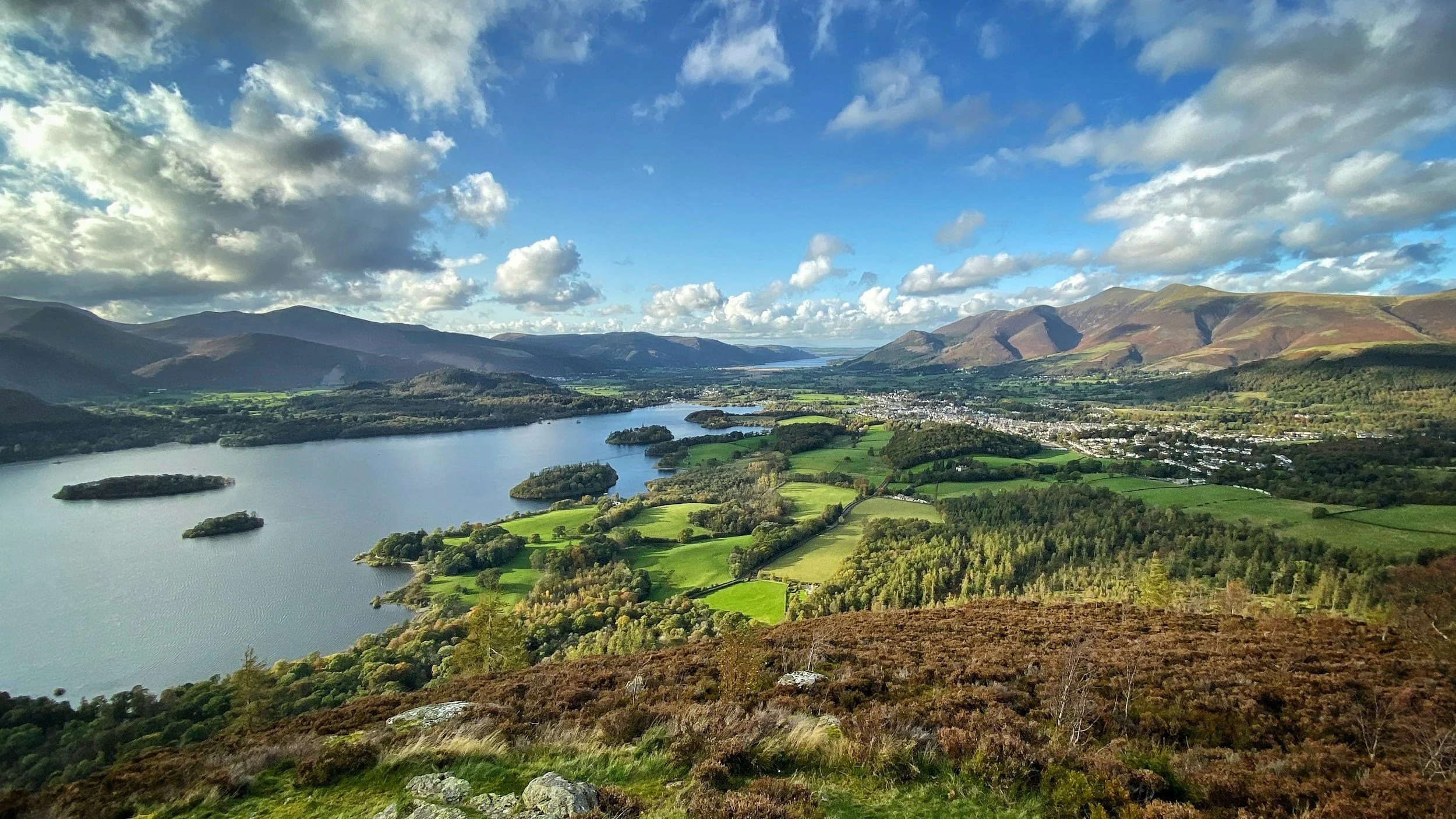 A scenic view of a river with small islands, surrounded by green fields and hills under a partly cloudy sky.
