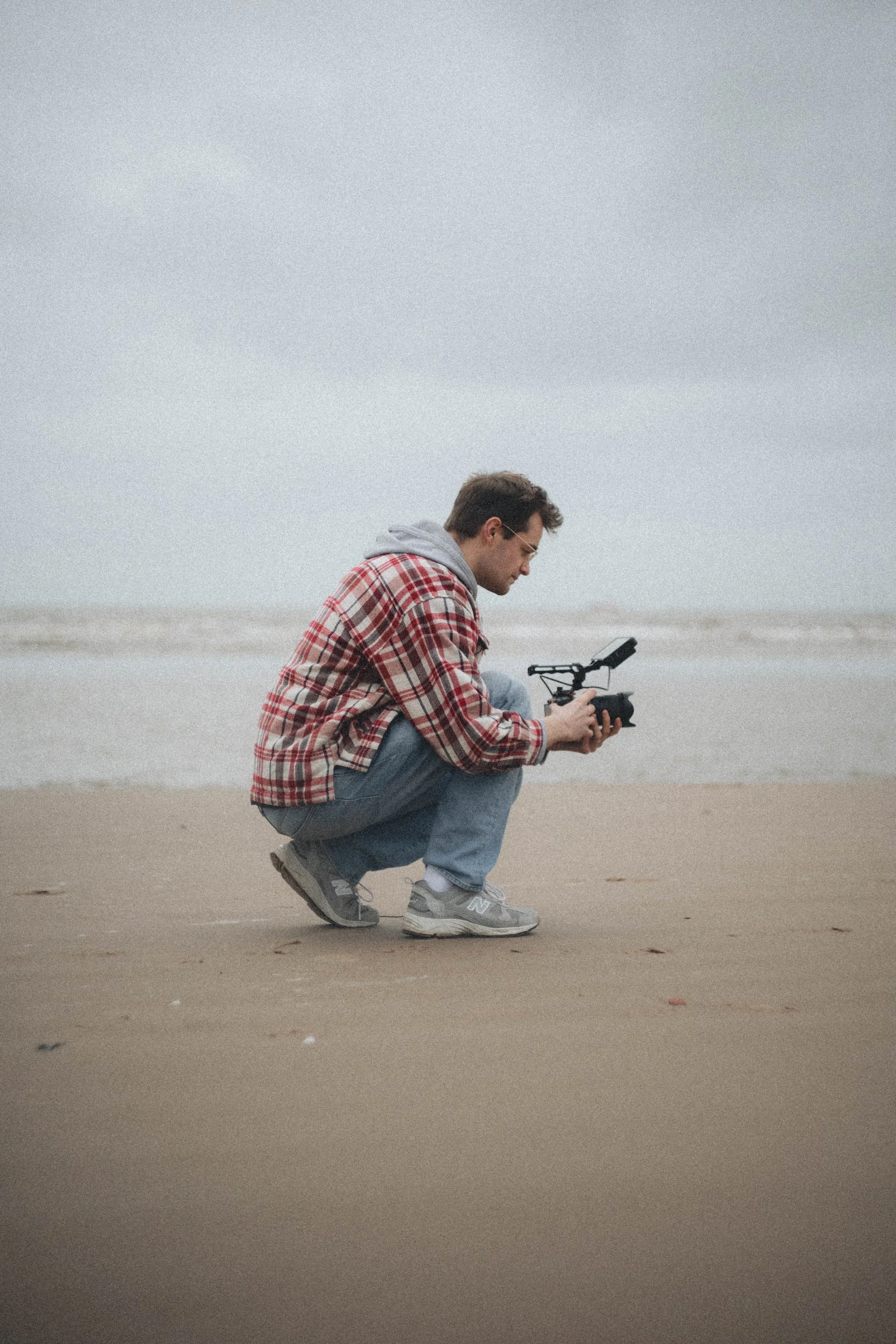 A man squatting on the beach examining a drone he is holding.