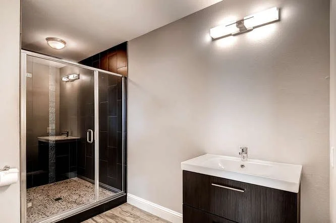 Modern bathroom with walk-in shower, sink with dark wooden cabinet, and wall-mounted light fixture.