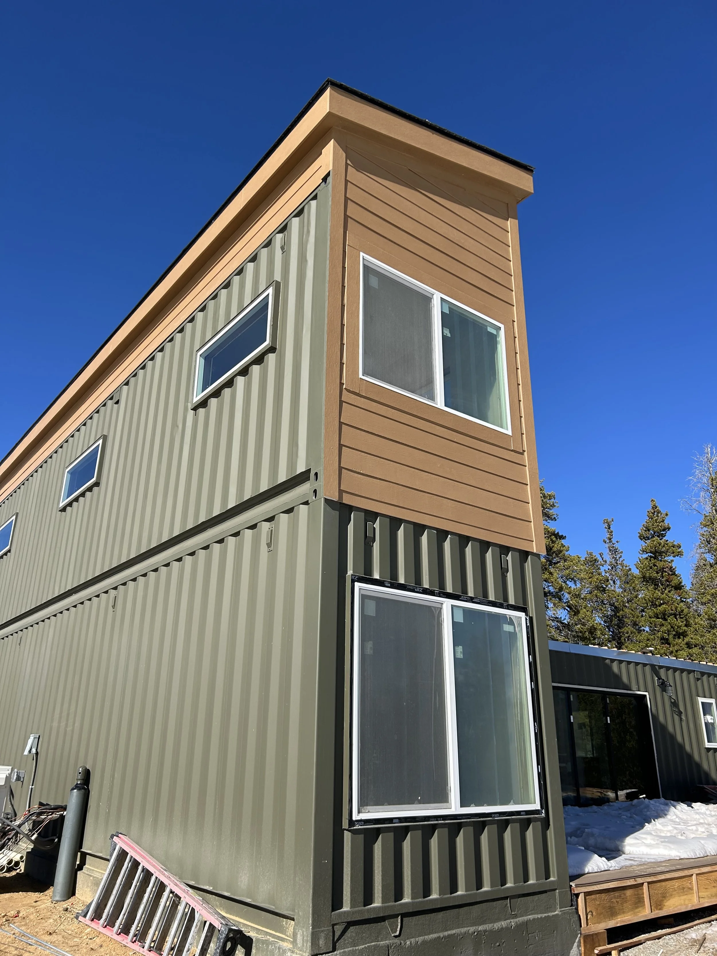 A modern two-story shipping container home with large windows and a clear blue sky background.