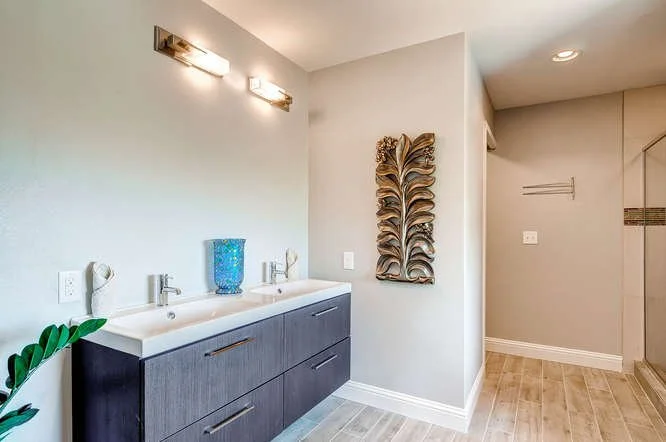 Modern bathroom with double sink vanity, decorative wall art, and light fixtures above mirror.
