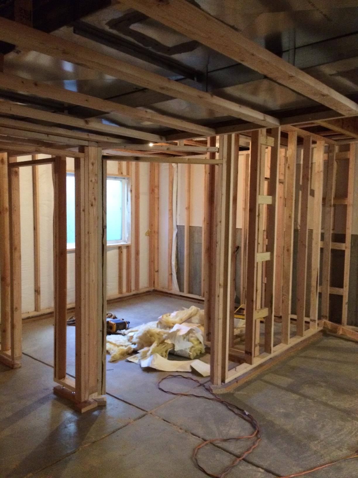 Interior of a house under construction with exposed wooden framing, insulation on the floor, and a window in the background.