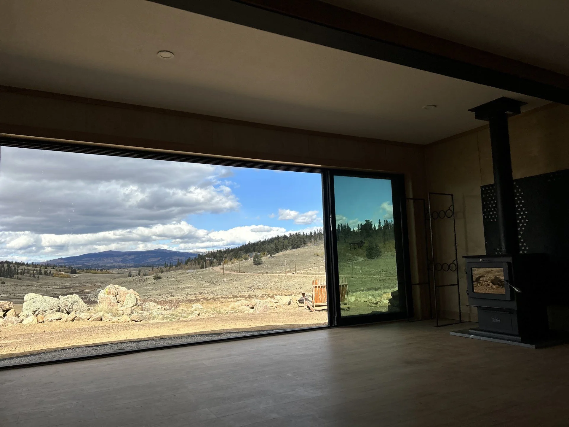 Interior of a room with a large glass window/view showing a landscape with mountains, clouds, and open land with rocks and trees.