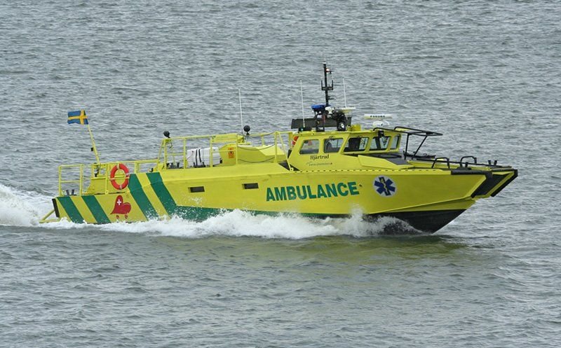 Yellow rescue boat marked as ambulance, speeding across water with Swedish flag at the stern.