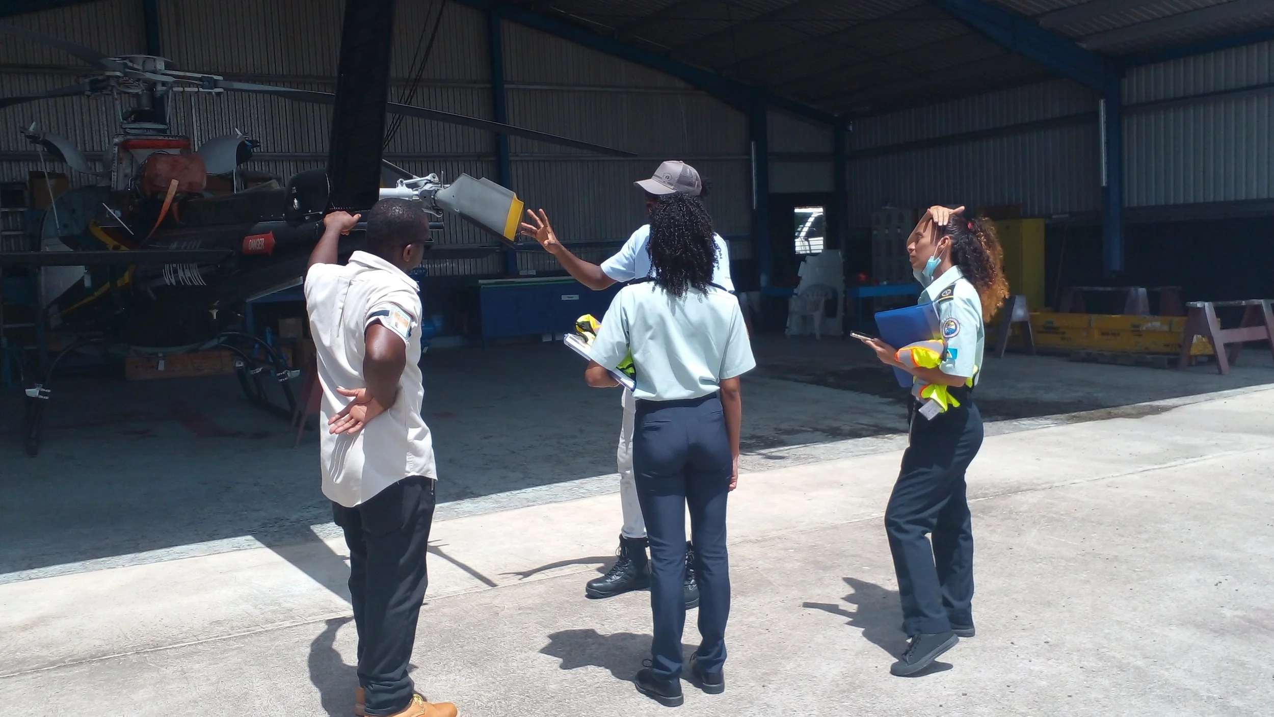 Four people, two women and two men, in a hangar near a helicopter engaged in a discussion about aviation or maintenance.