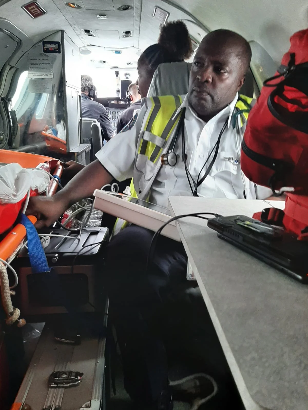 Medical professional in uniform and a yellow reflective vest inside a medical helicopter, attending to a patient.