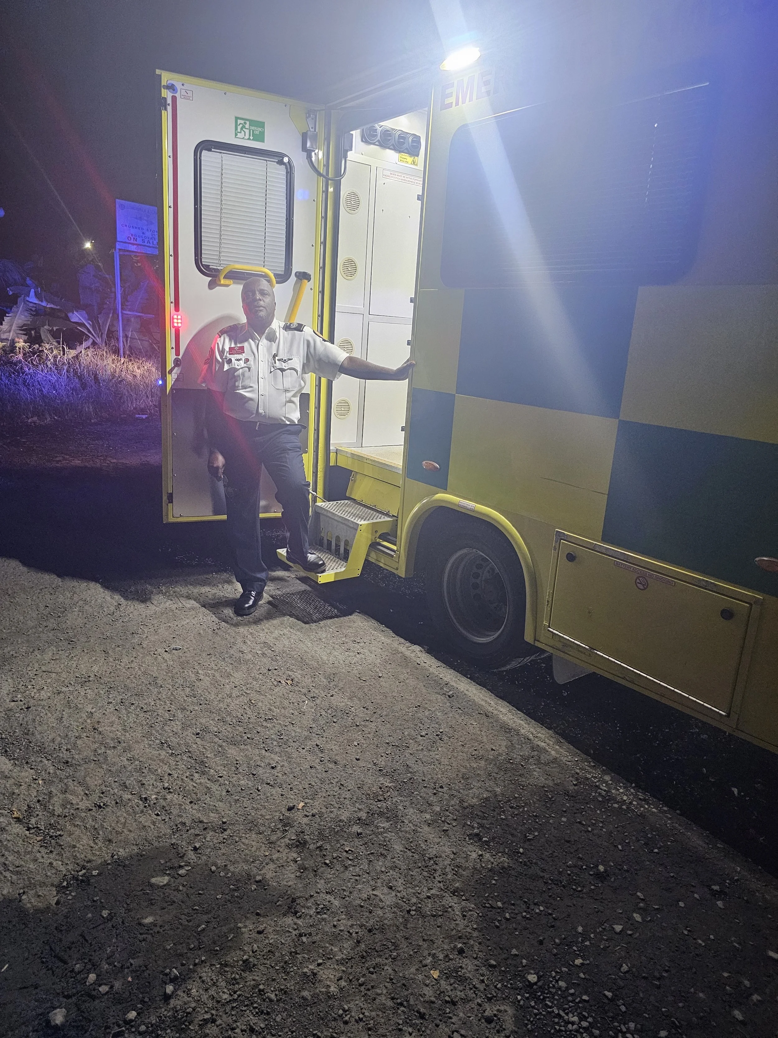 A man in a uniform standing outside a yellow and white ambulance at night.