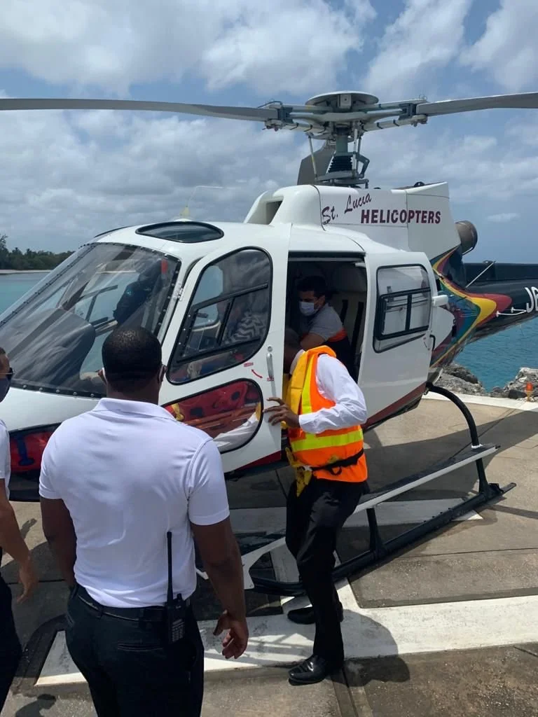 People boarding a helicopter on a dock near the ocean, with one person in a reflective vest.