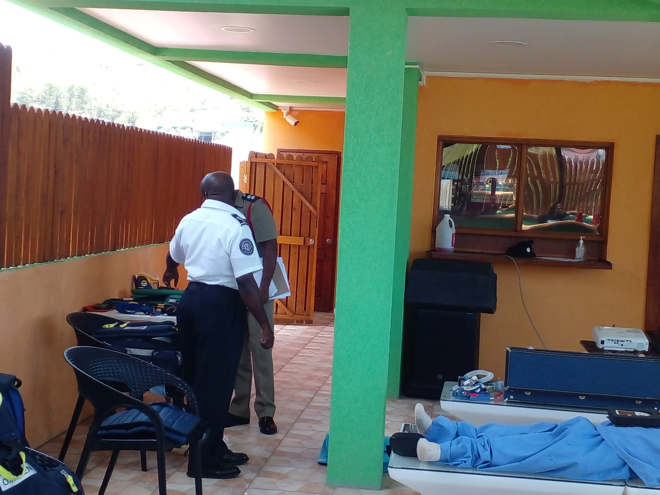 Emergency responders attending to a person lying on a hospital bed inside a room with yellow and green walls.