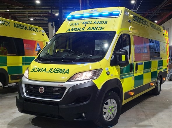 Yellow and green emergency ambulance vehicle with flashing blue lights parked indoors