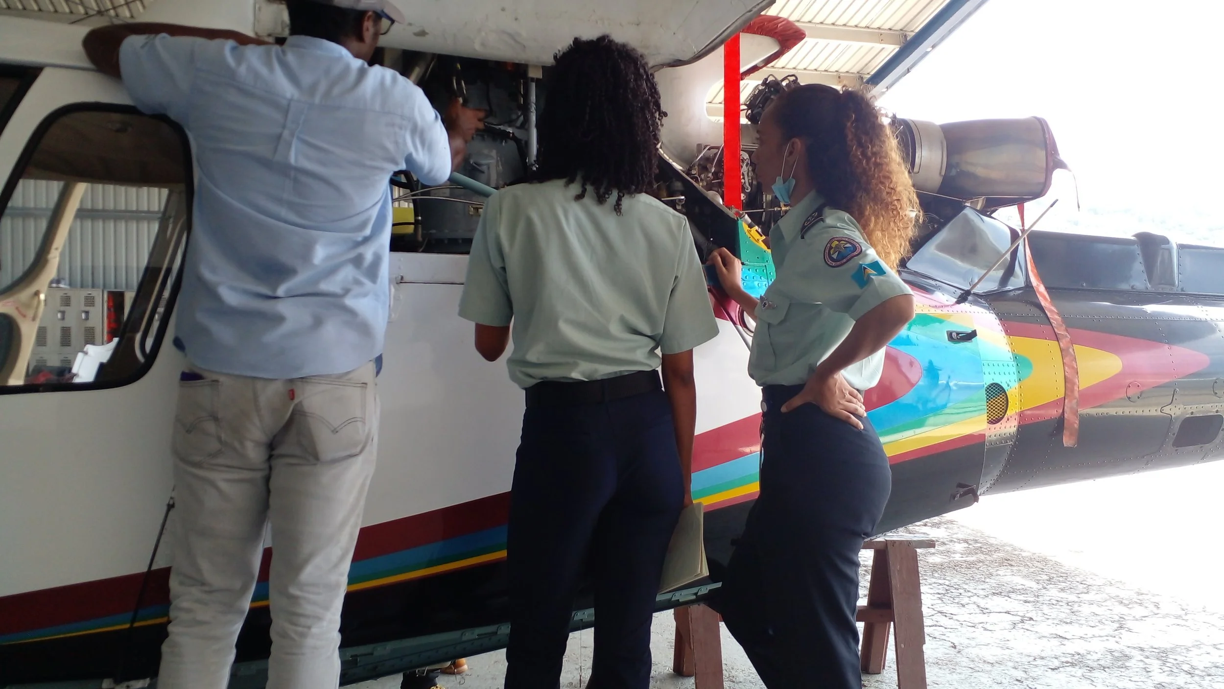 Three people in aviation uniforms working on a colorful helicopter inside a hangar.