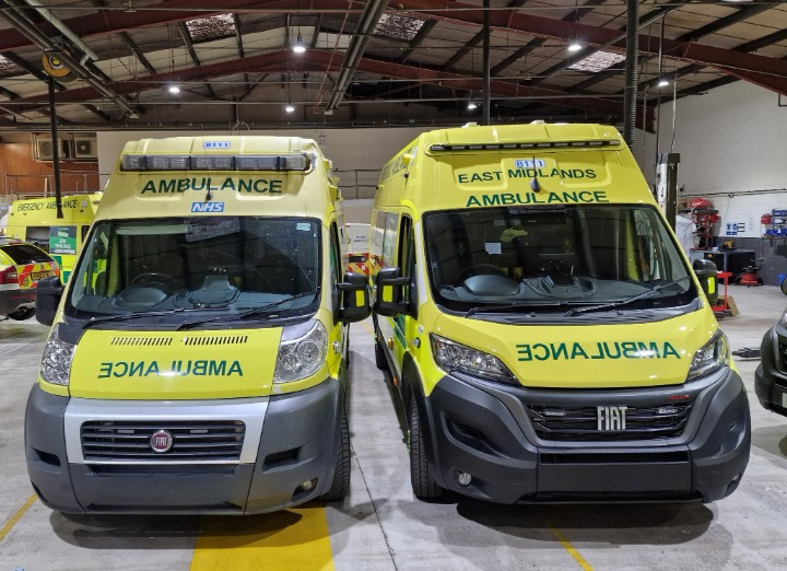 Two yellow and gray ambulances, one Fiat and one Fiat, parked inside a garage with vehicles and equipment in the background.