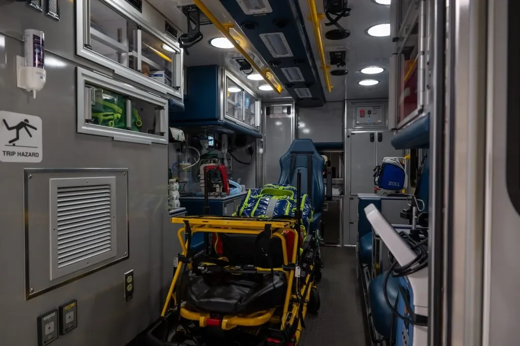 Inside an ambulance with medical equipment, a blue seat, and a stretcher with medical supplies.