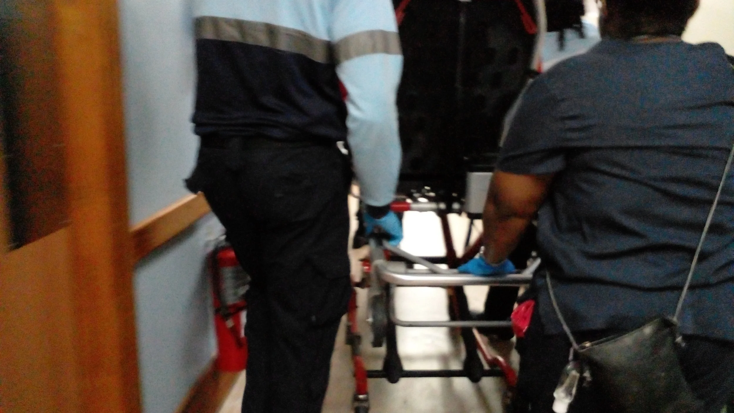 Two emergency responders in gloves and dark uniforms assisting a patient on a stretcher.