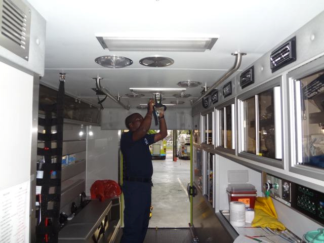 A technician installs or repairs ceiling equipment inside a mobile medical or lab trailer.