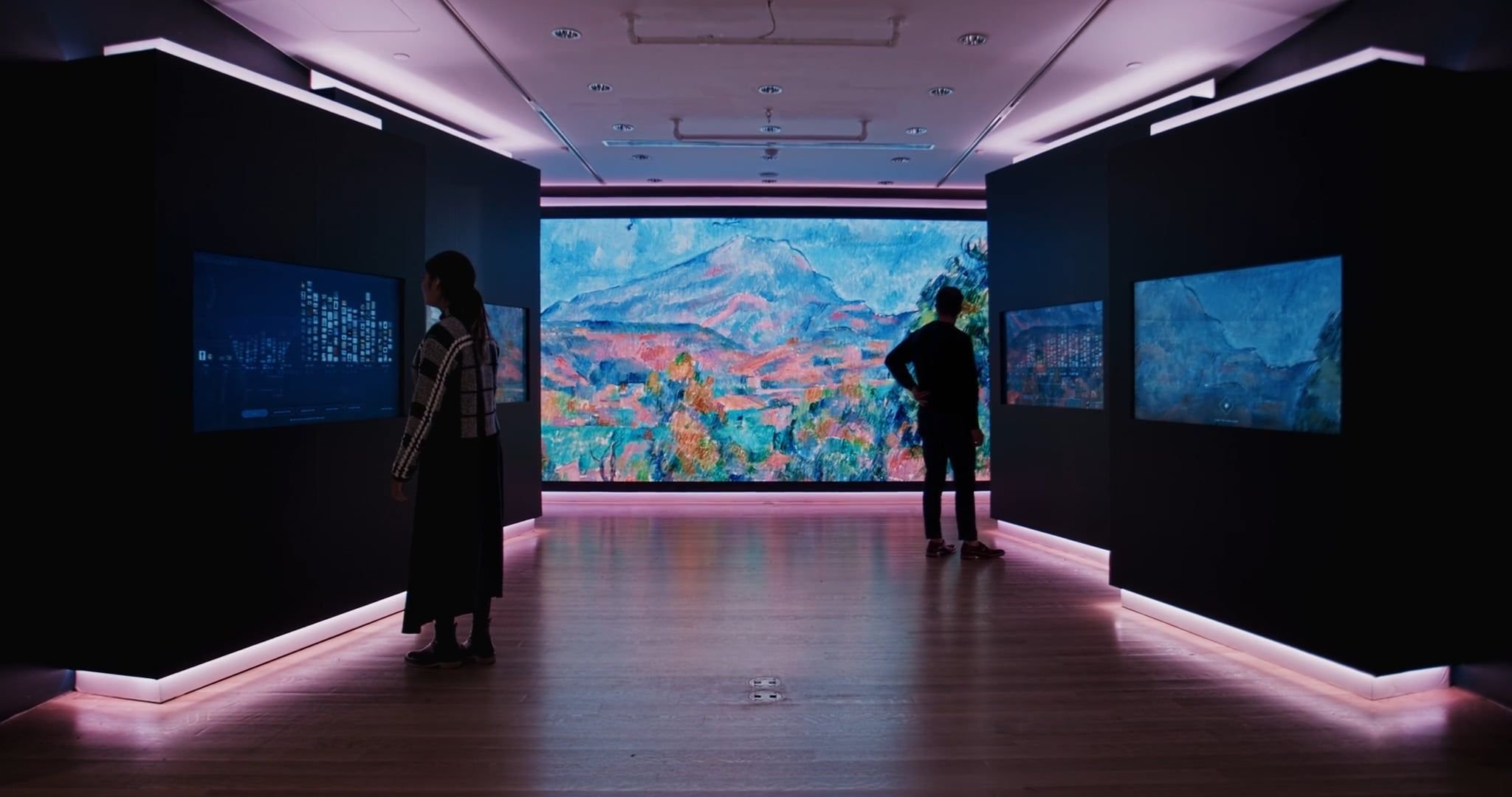 People viewing digital screens and a large landscape painting in an art gallery with pink lighting.