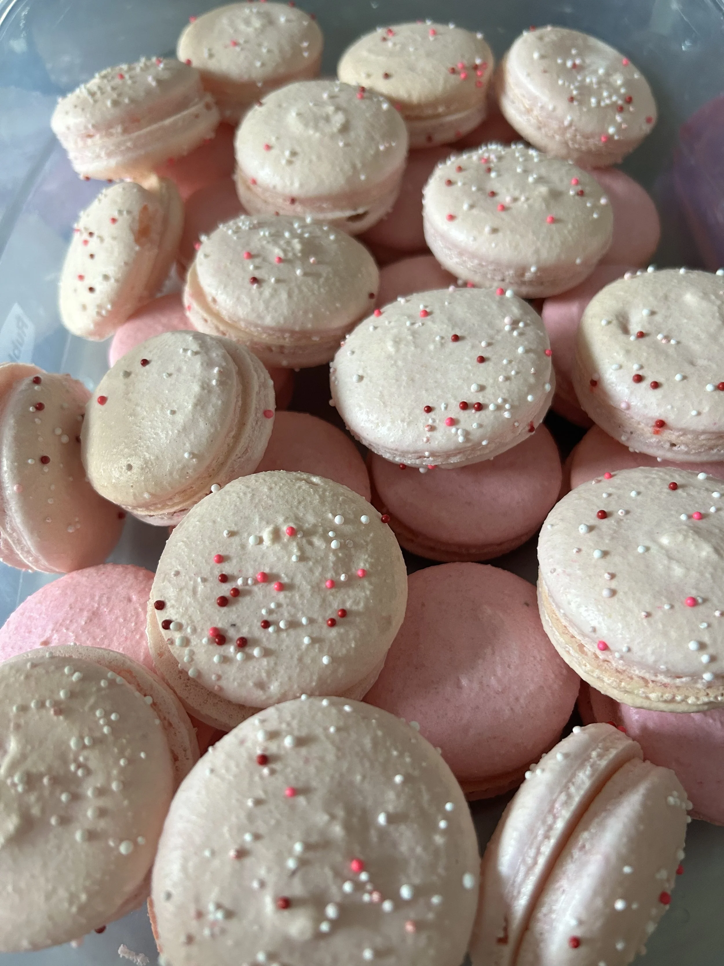 A plastic tray filled with pink and white macarons decorated with small pink, red, and white sprinkles.