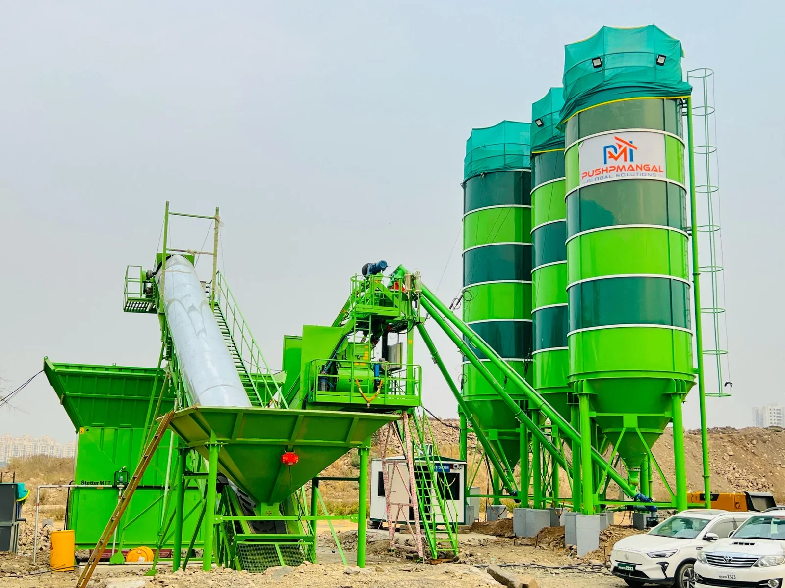 Green industrial concrete batching plant with silos and conveyor system on construction site.