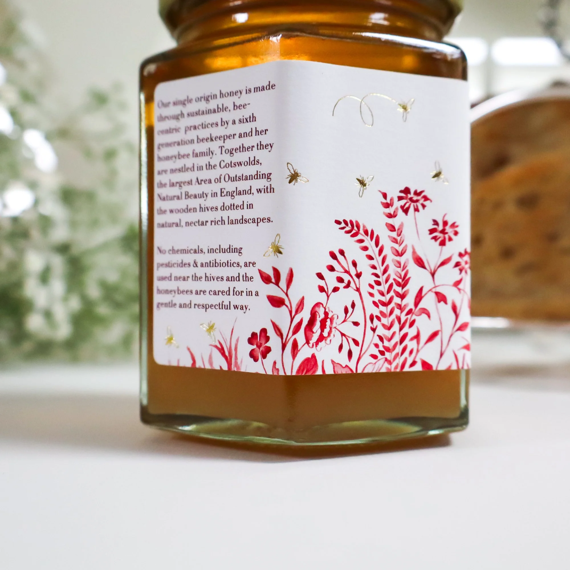 Close-up side view of a beautiful luxury labelled jar of ethical honey with white flowers and silver toast rack in the background.