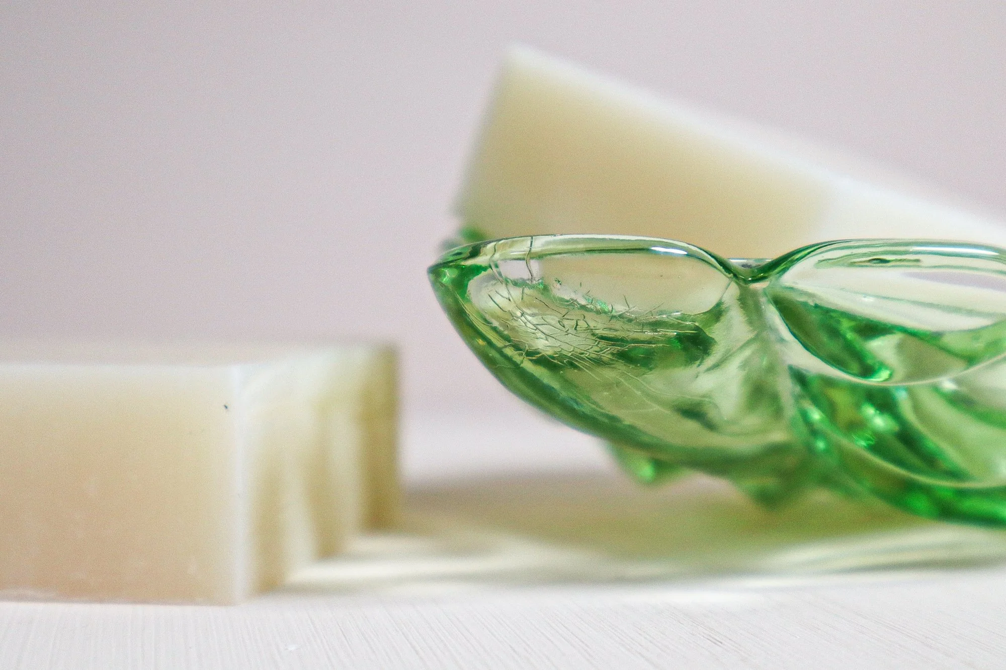 An up close photo of a beautful green glass dish with a bar of soap in it and a bar of soap laying next to it.