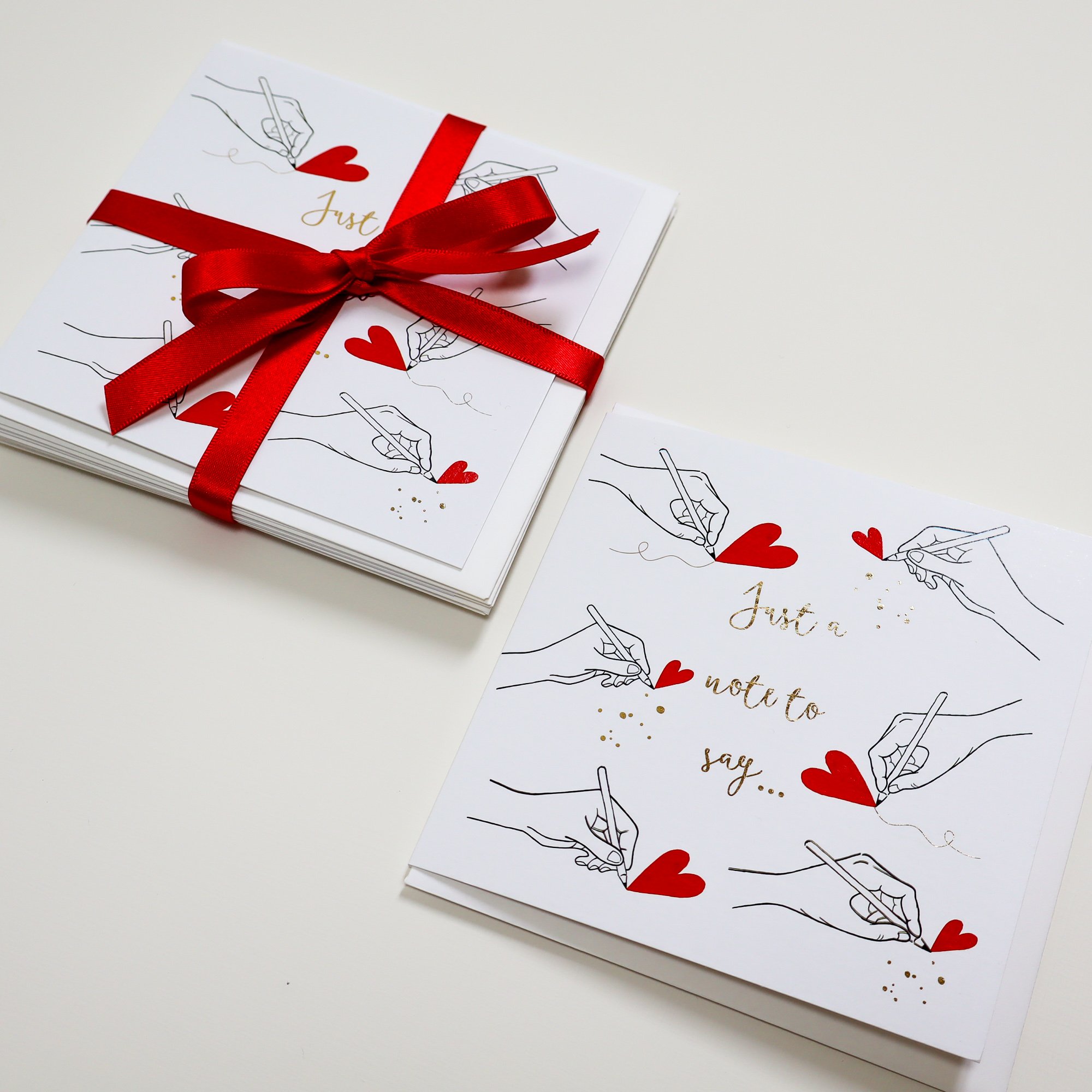 An aerial view of a pack of eco greeting cards wrapped in a red recycled yarn ribbon sitting next to a single card of the same design.