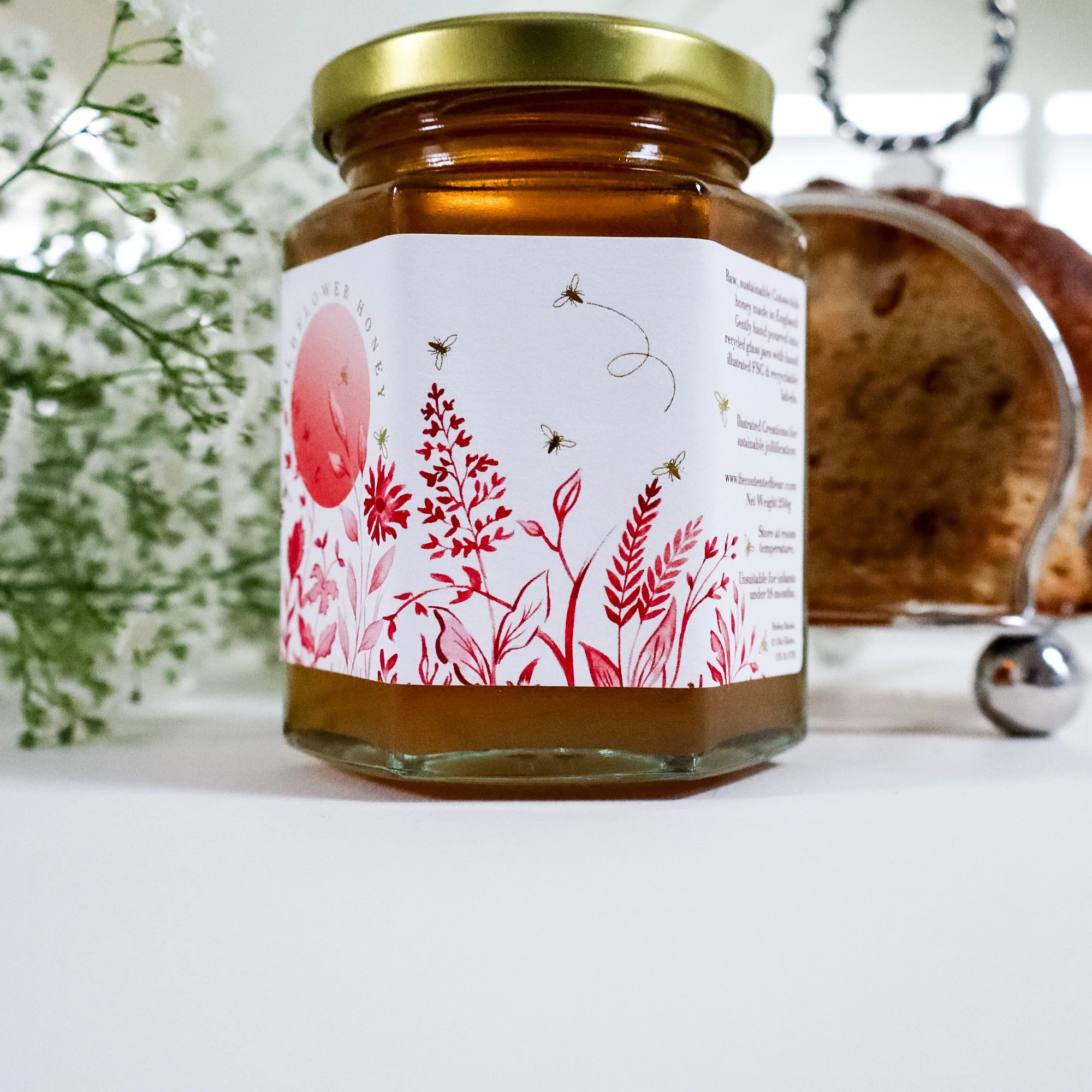 Side view of a beautiful illustrated honey jar with white flowers and silver toast rack in the background.